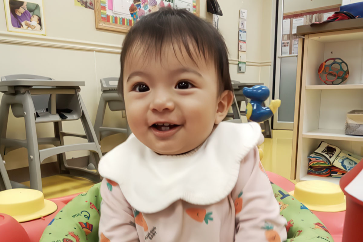 Smiling baby in a daycare setting surrounded by colorful toys and cheerful decor.